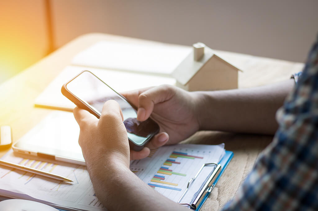 A person uses a smartphone while seated at a desk with financial charts